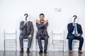 Businesspeople sitting in queue and waiting for interview, holding question marks in office Royalty Free Stock Photo