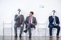 Businesspeople sitting in queue and waiting for interview, holding question marks in office Royalty Free Stock Photo