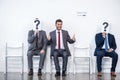 Businesspeople sitting in queue and waiting for interview, holding question marks in office Royalty Free Stock Photo