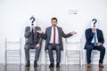 Businesspeople sitting in queue and waiting for interview, holding question marks in office Royalty Free Stock Photo