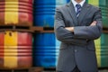 businessperson with arms crossed in front of oil barrels