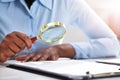 Businessperson Looking At Contract Form Through Magnifying Glass