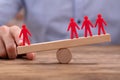 Businessperson Showing Imbalance Between Red Figures On Seesaw