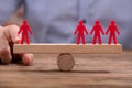 Businessperson Showing Imbalance Between Red Figures On Seesaw