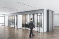 Businessperson walking in modern concrete glass office interior with daylight, equipment and wooden flooring. Workplace design