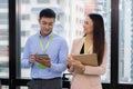 Businesss team leaning against the window. Woman looking at man and smile in the modern high level building. Man holding tablet