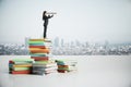 Businesswoman with binoculars standing on book pile