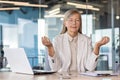 Businesswoman boss meditating with eyes closed at workplace inside office, senior woman working with laptop resting Royalty Free Stock Photo