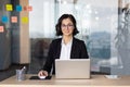 Businesswoman in business suit inside office working with laptop, woman smiling and looking at camera, female worker in Royalty Free Stock Photo