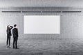 Businesswoman and businessman in gallery interior looking on blank banne