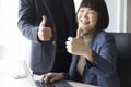 Businesswoman and businessman showing thumbs up sign with computer on wooden table in office background. Royalty Free Stock Photo