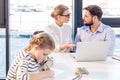 Businesswoman and businessman working with laptop in office with little daughter drawing on foreground Royalty Free Stock Photo