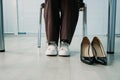 Businesswoman changing uncomfortable black high heels on comfortable white sneakers in office. Royalty Free Stock Photo