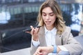 Businesswoman checks time on digital watch and records voice message, arranges a meeting, sits outside in city centre