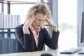 A businesswoman with curly blonde hair resting her hands on her head, feeling anxious, serious and tired Royalty Free Stock Photo