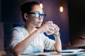 Businesswoman in eyeglasses holding cup while working late in office Royalty Free Stock Photo