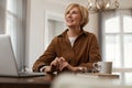 Businesswoman. Female With Laptop. Mature Blonde Woman In Brown Jacket Sits At The Desk With Computer And Cup.