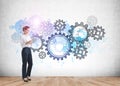 Businesswoman in formal wear holding tablet device. Parquet floor and concrete wall with colourful cogwheels and gears doodle.