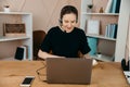 Businesswoman in headphones sits at desk, looks at laptop screen, making notes, participating in self-improvement webinar, having Royalty Free Stock Photo