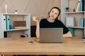 Businesswoman in headphones sits at desk, looks at laptop screen, making notes, participating in self-improvement webinar, having Royalty Free Stock Photo