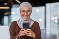 Businesswoman in hijab at work inside modern office close-up, Muslim woman using mobile phone, typing message and Royalty Free Stock Photo