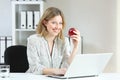 Businesswoman holding an apple looking at you at office