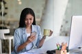 Businesswoman holding coffee cup and checking news on smart phone in office room.