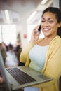 Businesswoman holding laptop while using mobile phone in cafeteria Royalty Free Stock Photo