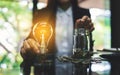 Businesswoman holding a light bulb over coins stack on the table while putting coin into a glass jar Royalty Free Stock Photo