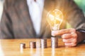 Businesswoman holding and putting lightbulb on coins stack on table for saving money concept Royalty Free Stock Photo