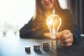 Businesswoman holding and putting lightbulb on coins stack on table Royalty Free Stock Photo