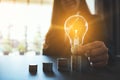 Businesswoman holding and putting lightbulb on coins stack on table