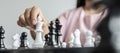 Businesswoman holding white chess pieces on a chessboard, comparing chessboard to business administration.