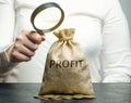 Businesswoman holds a magnifying glass over a money bag with the word Profit. Analysis of the budget in the company. Revenue