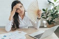 businesswoman in hot office with laptop and documents blowing herself