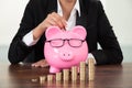 Businesswoman inserting coin in piggybank at desk