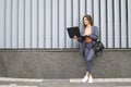 Businesswoman with laptop stay in the city against the background of the wall, a girl in a striped suit using computer outdoors