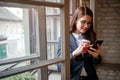 Businesswoman looking at cell phone by window