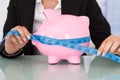 Businesswoman measuring piggybank at desk