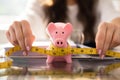 Businesswoman Measuring Piggybank With Measuring Tape