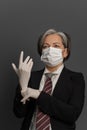 Businesswoman in medical mask putting on white disposable gloves. Wise mature woman complies with safety measures due to