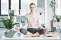 Businesswoman meditating in lotus position on messy table in office