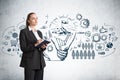 Businesswoman with notebook, light bulb with gears drawing on grey wall Royalty Free Stock Photo
