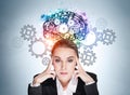 Businesswoman with pensive look, gears and colourful brain sketch on blue wall Royalty Free Stock Photo