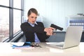 Businesswoman pointing gun to computer laptop sitting at desk desperate and stressed Royalty Free Stock Photo