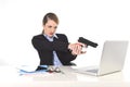 Businesswoman pointing gun to computer laptop sitting at office desk desperate and stressed Royalty Free Stock Photo