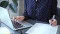 Businesswoman professional writing in a notebook beside a laptop at a modern bright office, close up view. Business