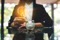 A businesswoman putting light bulb over a piggy bank on pile of coins on the table for saving money Royalty Free Stock Photo