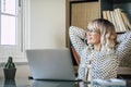 Businesswoman relaxing on chair with hands behind head while working on laptop at office. Caucasian young woman looking out Royalty Free Stock Photo