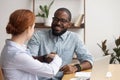 Businesswoman shaking hand of African American colleague at workplace Royalty Free Stock Photo